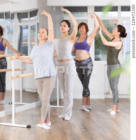 Elderly woman learning third ballet position at beginners class with instructor 128471380