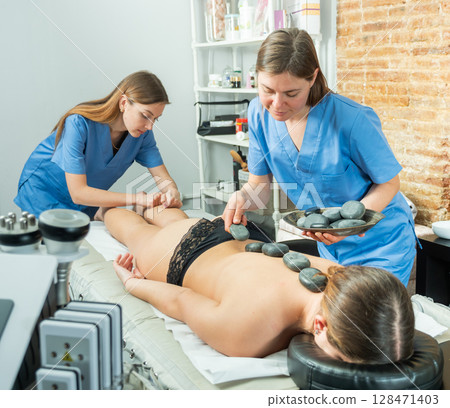 Two masseuses massage the legs and perform a stone therapy procedure Two masseuses massage the legs and perform a stone therapy procedure 128471403