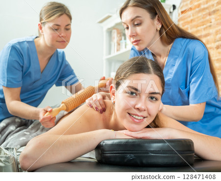 Smiling girl getting professional maderotherapy from two masseuse 128471408