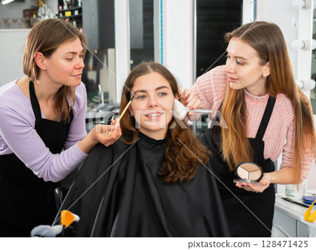 Two female makeup artists working with young girl client Two female makeup artists working with young girl client 128471425