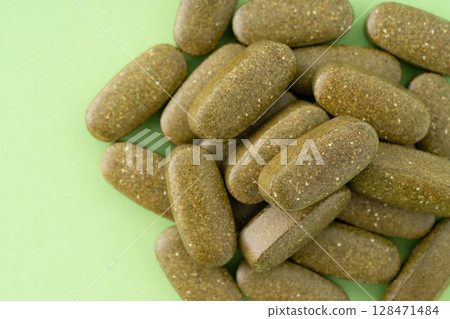 Khaki supplement pills (oval shape) on a green background 128471484