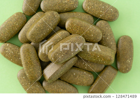 Khaki supplement pills (oval shape) on a green background 128471489