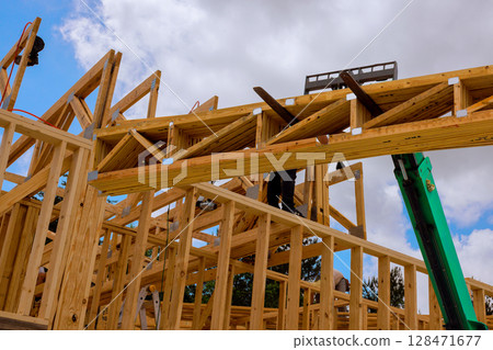 Skilled workers use cranes ladders to erect wooden beams for residential structure in progress under telehandler lifting 128471677