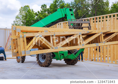 Workers use telehandler to lift wooden frames at construction site amidst trees, showcasing teamwork in action. Workers use telehandler to lift wooden frames at construction site amidst trees, showcasing teamwork in action. 128471843