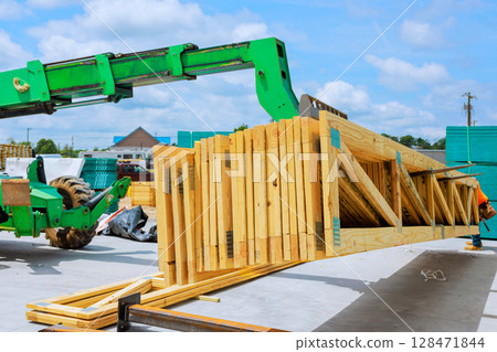 Construction worker uses green machine to lift wooden beams truss at site under works day time. 128471844