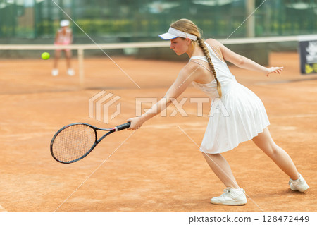 Female athlete plays tennis on open court 128472449