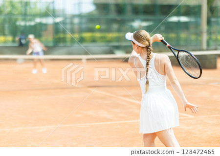 Concentrated sporty girl with tennis racquet and ball in her hands standing and ready to play match standing 128472465