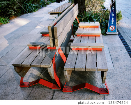 A striking red public wooden bench on a city sidewalk A striking red public wooden bench on a city sidewalk 128474224