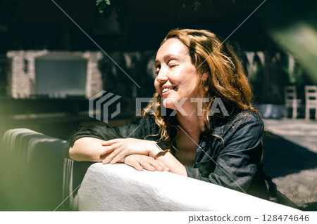 Happy Woman Enjoying Sunlight Outdoors with Closed Eyes and Relaxed Smile in Cozy Garden Cafe Happy Woman Enjoying Sunlight Outdoors with Closed Eyes and Relaxed Smile in Cozy Garden Cafe 128474646