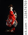 Japanese Geisha doll dressed in a beautiful kimono, on black background. 128474769