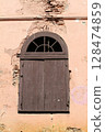 Old brown wooden window under steel arched lintels on a cracked brick wall. 128474859