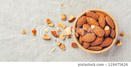 Almonds in wooden bowl with broken almond on linen table cloth background Almonds in wooden bowl with broken almond on linen table cloth background 128475626