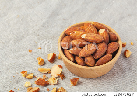 Roasted almonds in wooden bowl on linen table cloth background Roasted almonds in wooden bowl on linen table cloth background 128475627