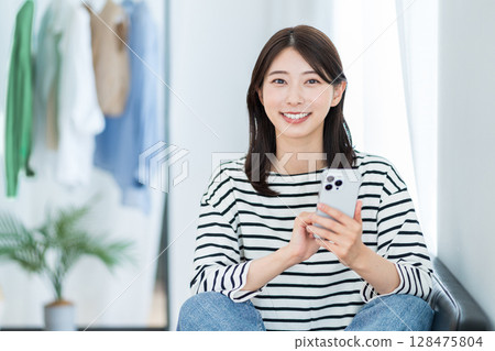 一名年輕女子在她的房間裡使用智慧型手機。 128475804