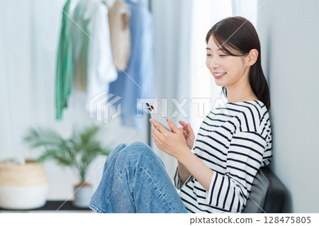 一名年輕女子在她的房間裡使用智慧型手機。 128475805