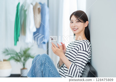 A young woman using a smartphone in her room. 128475809