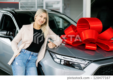 Saleswoman Leaning on New Car with Red Bow in Dealership 128477167