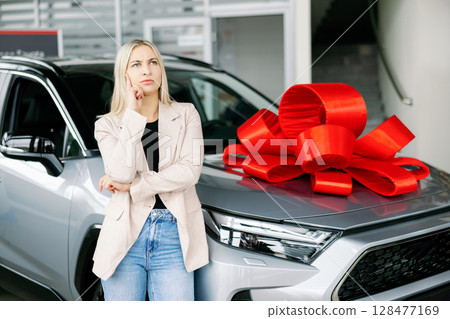 Thoughtful businesswoman choosing new car in dealership showroom Thoughtful businesswoman choosing new car in dealership showroom 128477169