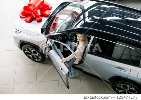 Happy business woman sitting in new car with red bow in dealership 128477175