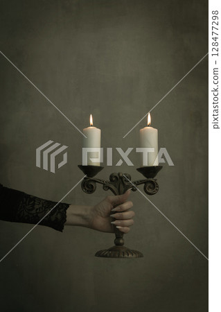 Female hand in black lace vintage sleeve hold old brass candelabrum with burning candles in the dark, vertical image. Female hand in black lace vintage sleeve hold old brass candelabrum with burning candles in the dark, vertical image. 128477298