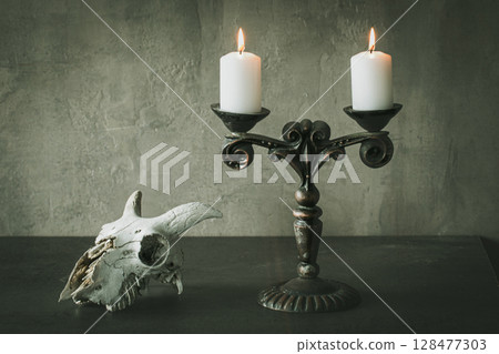 Beautiful vintage metal candelabrum with two burning candles and goats skull on the table, atmospheric image. 128477303