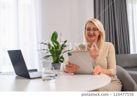 Middle aged professional woman in pleasant atmosphere offering online counseling, using notebook and tablet for mental wellness support. Middle aged professional woman in pleasant atmosphere offering online counseling, using notebook and tablet for mental wellness support. 128477556