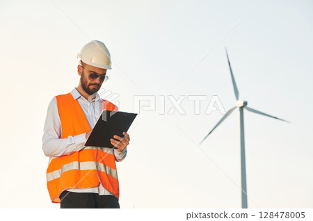 With notepad. Service engineer is on the field with windmills 128478005