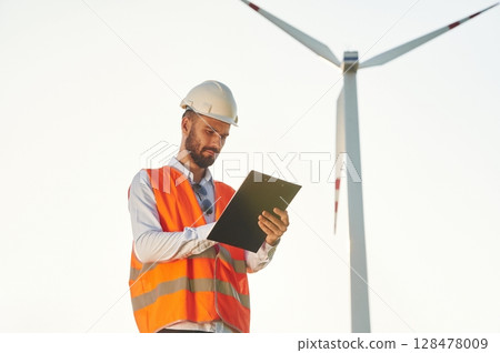 With notepad. Service engineer is on the field with windmills 128478009