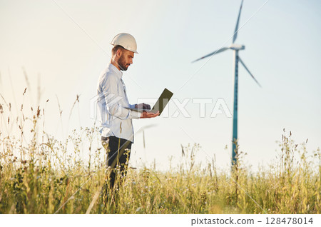 Working by using laptop. Service engineer is on the field with windmills 128478014