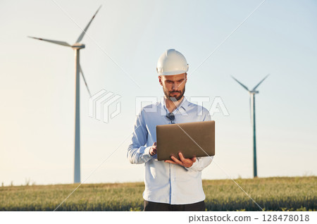 Working by using laptop. Service engineer is on the field with windmills Working by using laptop. Service engineer is on the field with windmills 128478018