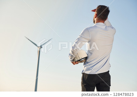 Rear view. Service engineer is on the field with windmills Rear view. Service engineer is on the field with windmills 128478023
