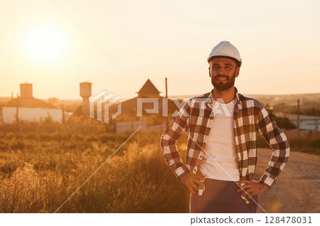 Man in hard hat is outdoors against sunset light. Rural scene 128478031