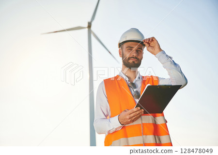Black notepad in hands. Service engineer is on the field with windmills Black notepad in hands. Service engineer is on the field with windmills 128478049