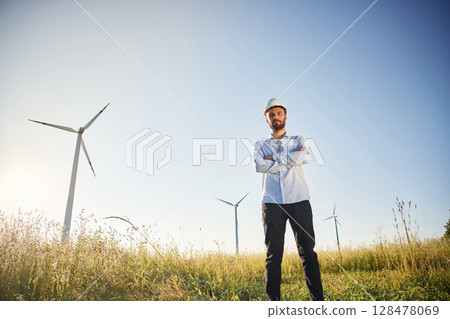 Handsome service engineer is standing on the field with windmills Handsome service engineer is standing on the field with windmills 128478069