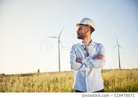 Handsome service engineer is standing on the field with windmills Handsome service engineer is standing on the field with windmills 128478071
