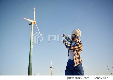Pointing to one of the turbines. Service engineer is on the field with windmills 128478132