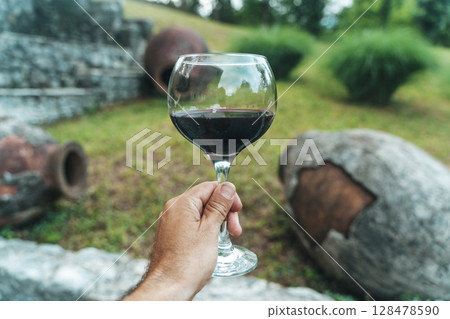 Glass of Red Wine with Traditional Georgian Qvevri in Rustic Setting 128478590