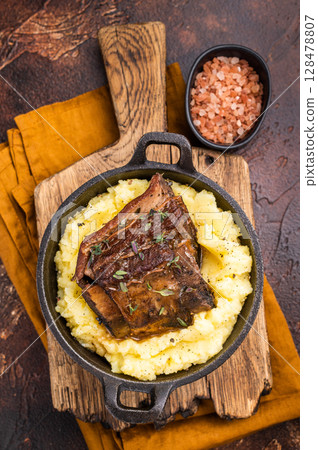 Close-up of tender beef short ribs, beautifully caramelized and resting on a bed of creamy mashed potatoes, creating an inviting culinary scene. brown background. top view 128478807
