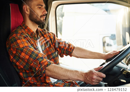 Side view, sitting inside the vehicle. Young truck driver in casual clothes 128479152