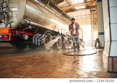 Fuel tanker is getting washing. Young truck driver in casual clothes Fuel tanker is getting washing. Young truck driver in casual clothes 128479208