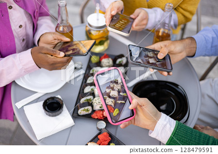 Friends gather at a table to take photos of sushi with their smartphones, capturing the moment of their meal together. 128479591