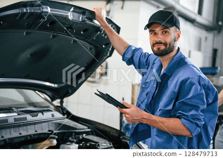 With tablet in hands. Auto mechanic working in garage. Repair service 128479713