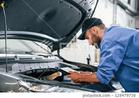 With tablet in hands. Auto mechanic working in garage. Repair service With tablet in hands. Auto mechanic working in garage. Repair service 128479716