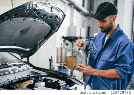 Oil can in hands. Auto mechanic working in garage. Repair service 128479720