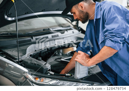 Grey colored oil can in hands. Auto mechanic working in garage. Repair service Grey colored oil can in hands. Auto mechanic working in garage. Repair service 128479734