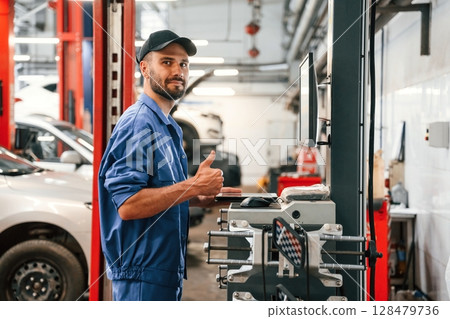 Standing by computer terminal. Auto mechanic working in garage. Repair service 128479736
