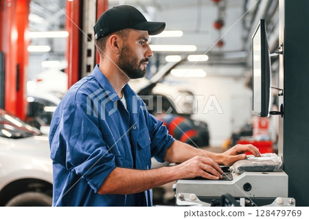 In black cap. Using computer. Auto mechanic working in garage. Repair service 128479769