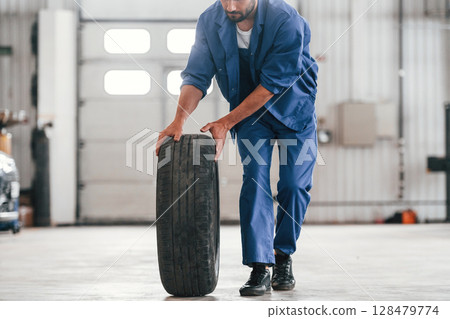 Walking with new tire. Auto mechanic working in garage. Repair service 128479774