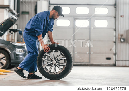 Side view. Moving the new tire. Auto mechanic working in garage. Repair service Side view. Moving the new tire. Auto mechanic working in garage. Repair service 128479776