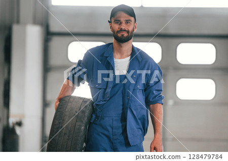 Tire in hand. Auto mechanic working in garage. Repair service Tire in hand. Auto mechanic working in garage. Repair service 128479784